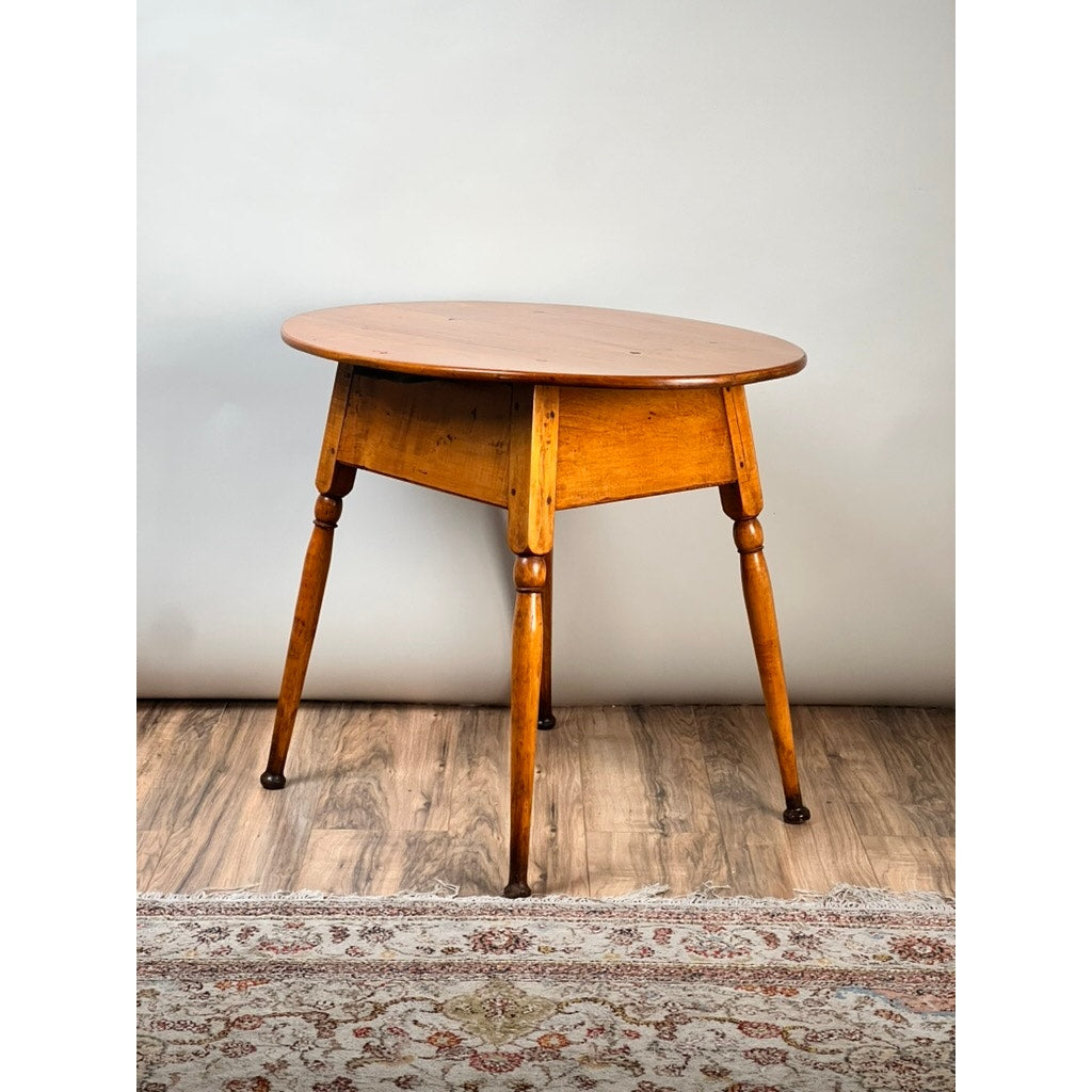 An Antique American Queen Anne Maple Tavern Table from New England (circa 1760–1790) with tapered legs stands on a wood floor beside a patterned rug, set against a plain light-colored wall.