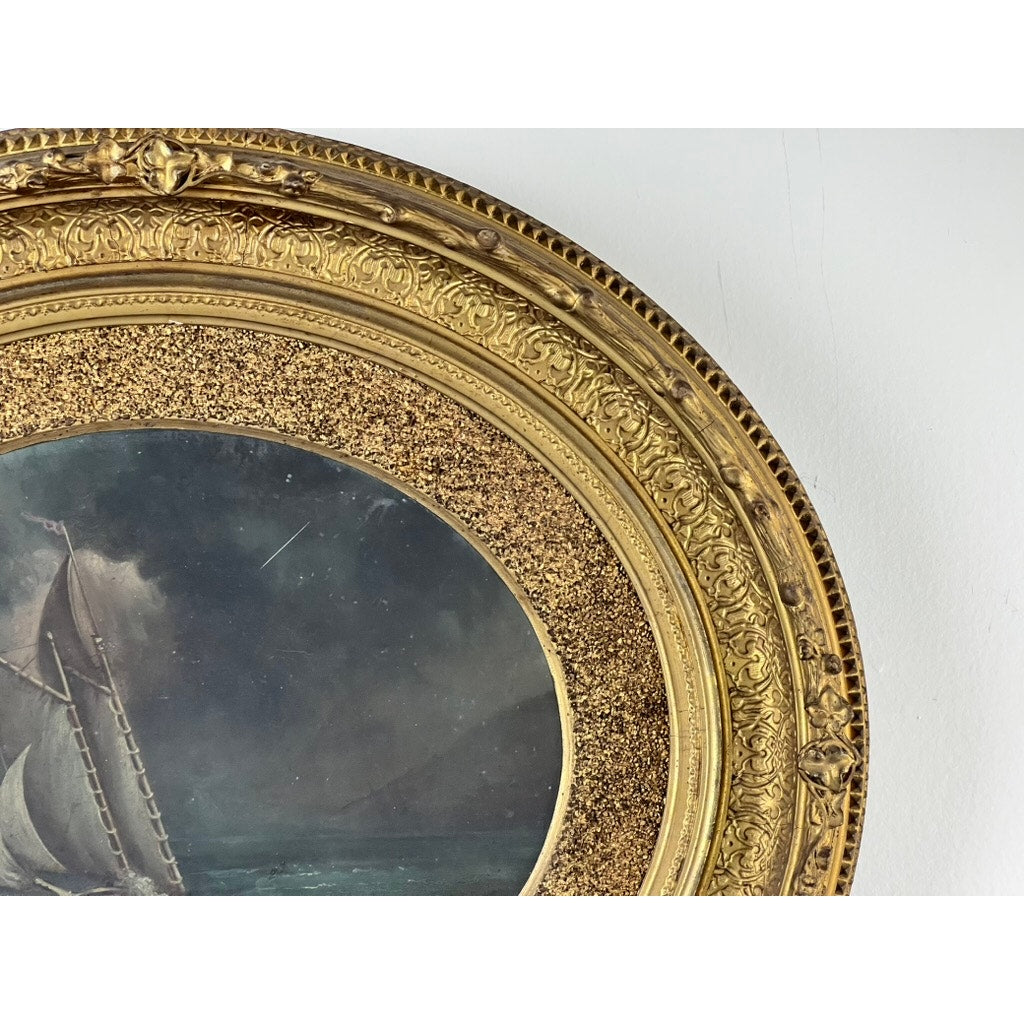 A close-up of the ornate, antique gilt frame of an oval “Storm Tossed Ship” oil on board painting (late 19th century), featuring a detailed maritime scene of a ship battling stormy night waters.
