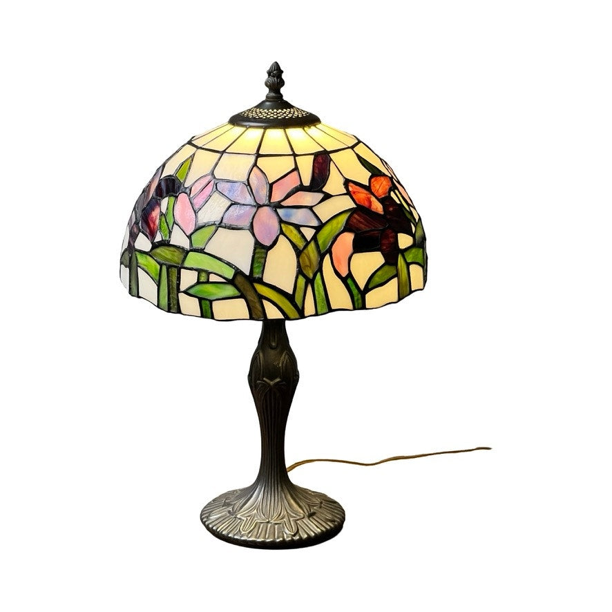 The Vintage Tiffany Style Floral Stained Glass Table Lamp features a colorful floral shade with green stems, an ornate metal base, and a visible power cord for easy use. Brand is unknown.