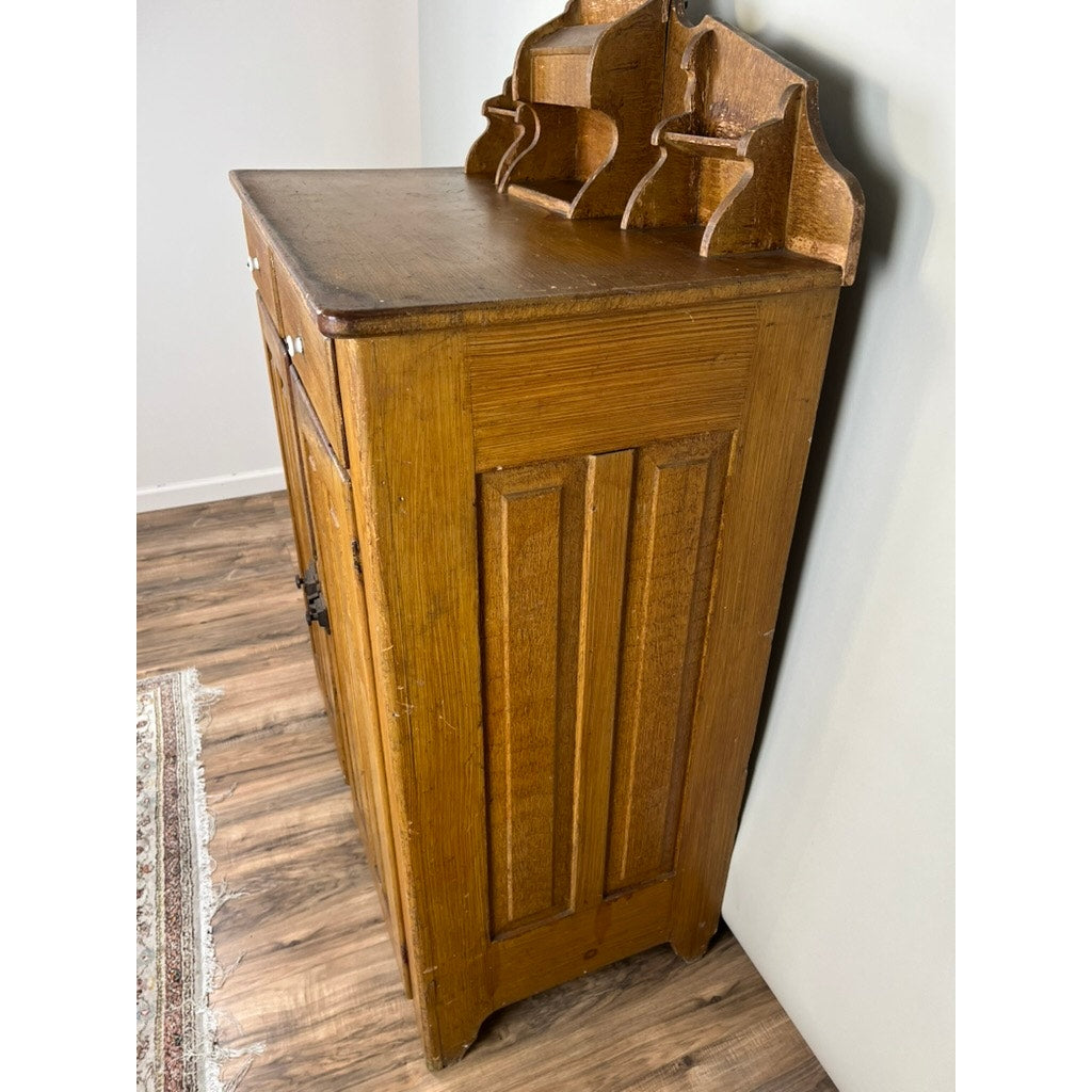 An Antique Victorian Country Grain Painted Jelly Cupboard c. 1870 with vertical panels, a flat top, and a tiered shelf with decorative dividers stands against a white wall on wood flooring beside a partial rug. Brand: Unknown.