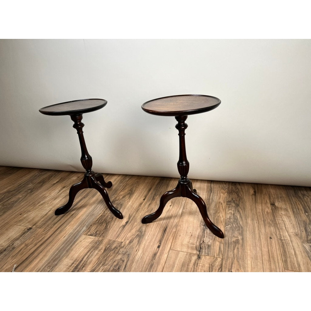 A vintage pair of diminutive walnut candle stands from circa 1940, each with a round top, slender central column, and three curved legs, stands on a light wood floor against a plain white wall.