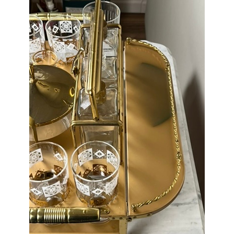 A Vintage Mid Century Modern Bar Caddy c. 1960s holds patterned glasses, a gold ice bucket with matching tongs, and square glass bottles, all neatly arranged on a shiny gold tray. Brand: None and/or Unknown.