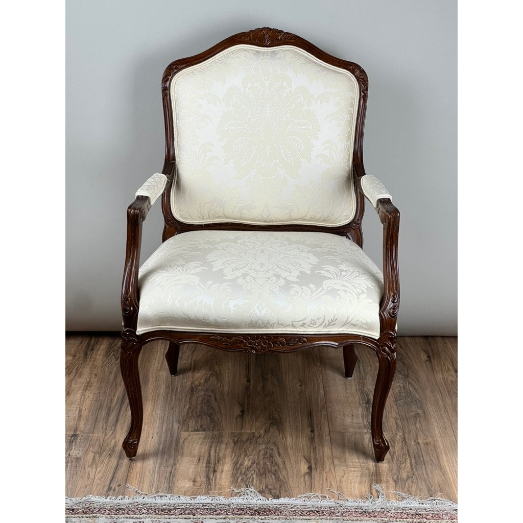A Vintage Louis XV Style Fauteuil Arm Chair by Pennsylvania House, featuring carved details and cream floral upholstery, stands on a wooden floor near a rug.
