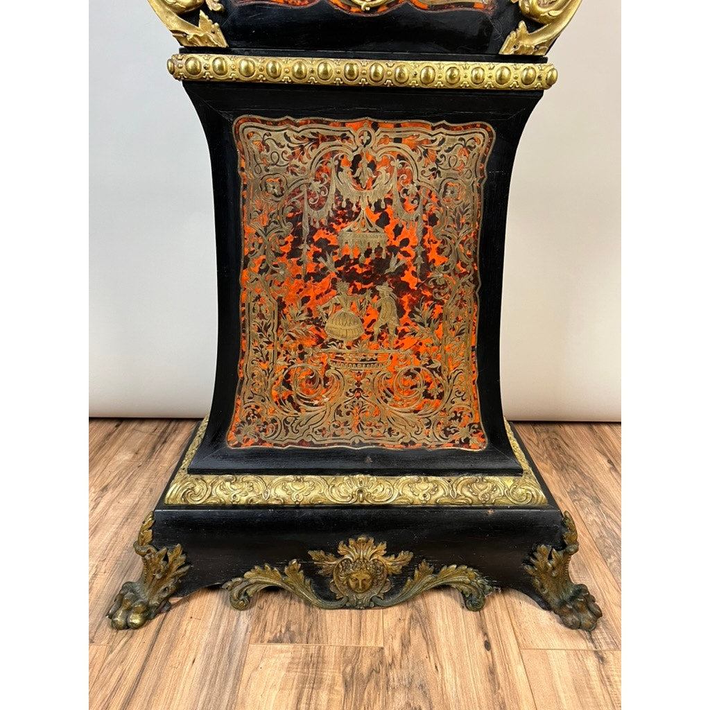 The image shows the ornate base of a Monumental French Napoleon III Boulle Marquetry Floor Clock with Ormolu Mounts, Circa 1865–1885, featuring decorative black and gold elements with intricate red and gold patterns, resting on a wooden floor—a striking example of Boulle marquetry that highlights the exquisite French decorative artistry of the era.