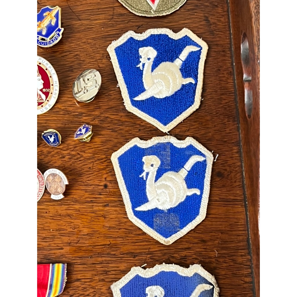 Two blue military patches with white ostrich emblems from the Attributed WWII 158th Infantry Bushmasters Grouping of Frank W. Slatcher, Company I, Pacific Theater, are displayed on wood with pins and related memorabilia.