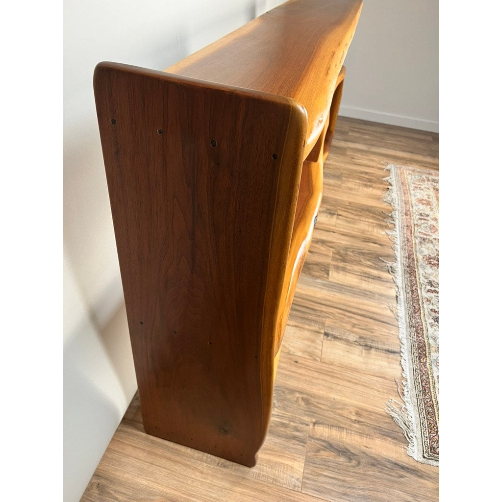 A wooden console table with smooth, rounded edges and natural grain stands against a wall near a rug, echoing the Vintage Mid-Century Modern Style Live Edge Walnut Bookshelf with its open shelf design.