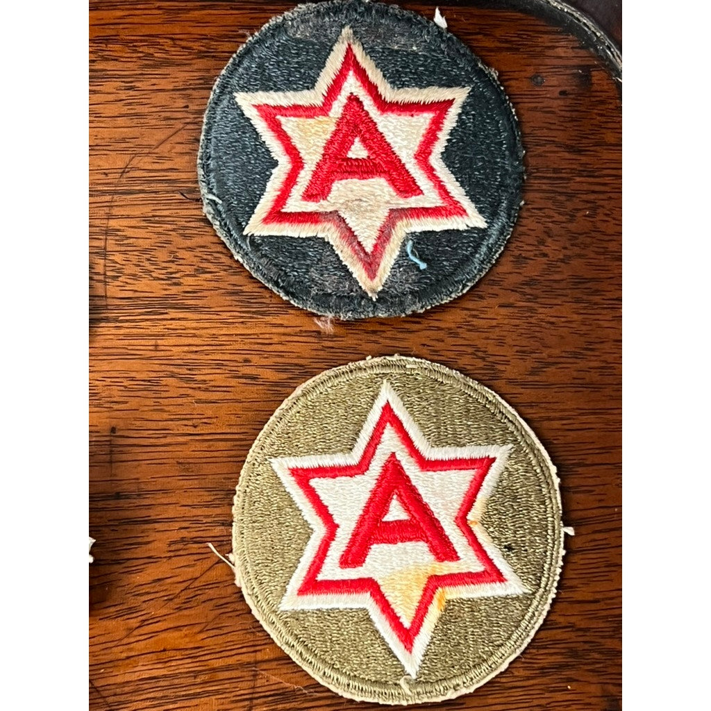 Two round fabric patches from the Attributed WWII 158th Infantry Bushmasters Grouping of Frank W. Slatcher, Company I, Pacific Theater—one dark blue, one olive green—each features a red "A" in a red/white six-pointed star on a wooden surface.