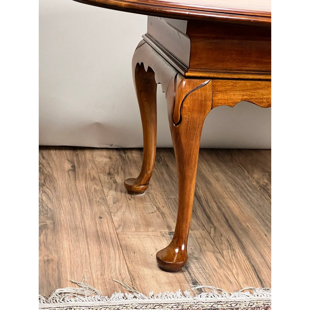 Close-up of a Vintage Solid Cherry Queen Anne Style Coffee Table attributed to Pennsylvania House, featuring curved polished legs on a wood floor beside a fringed rug, with a plain light-colored wall in the background.