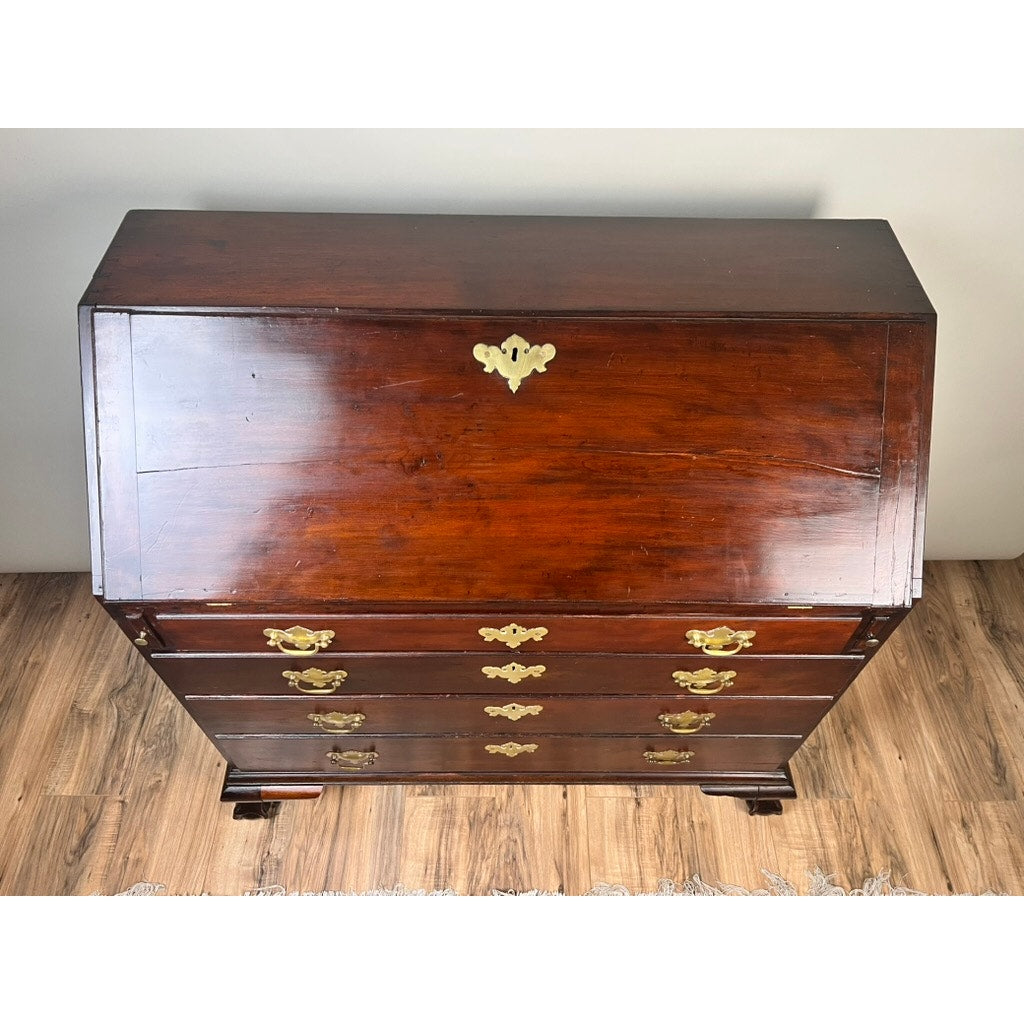 An 18th Century New England Chippendale Cherry Slant Front Desk, circa 1770–1790, with brass handles and a closed drop-front writing surface, sits gracefully on a hardwood floor, viewed from above.