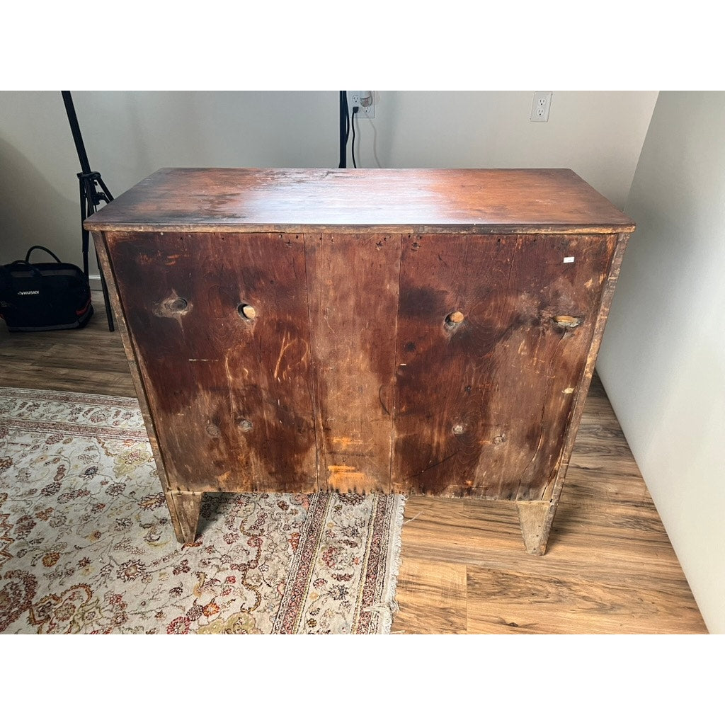 A rare labeled William Lloyd Springfield, Massachusetts Federal cherry chest of drawers, circa 1800, stands on a patterned rug in a room with wood flooring and white walls. The well-worn wooden chest shows visible scratches and stains, and several knobs are missing from the front, highlighting the craftsmanship typical of New England Federal furniture.