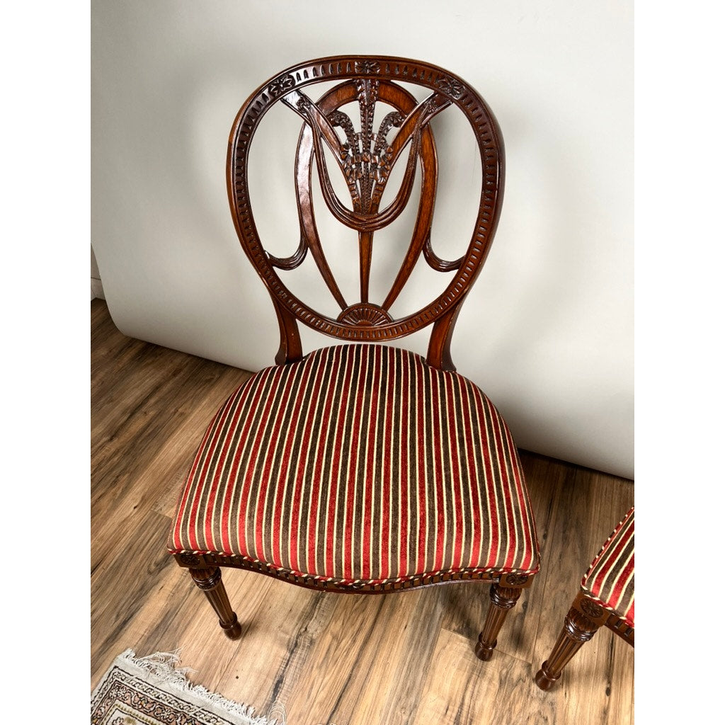A Vintage Pair of Wheel Back Side Chairs by Ardley Hall, featuring ornate carved backs and seats upholstered in red, green, and gold stripes. Set on a wooden floor beside a rug against a plain light-colored wall.