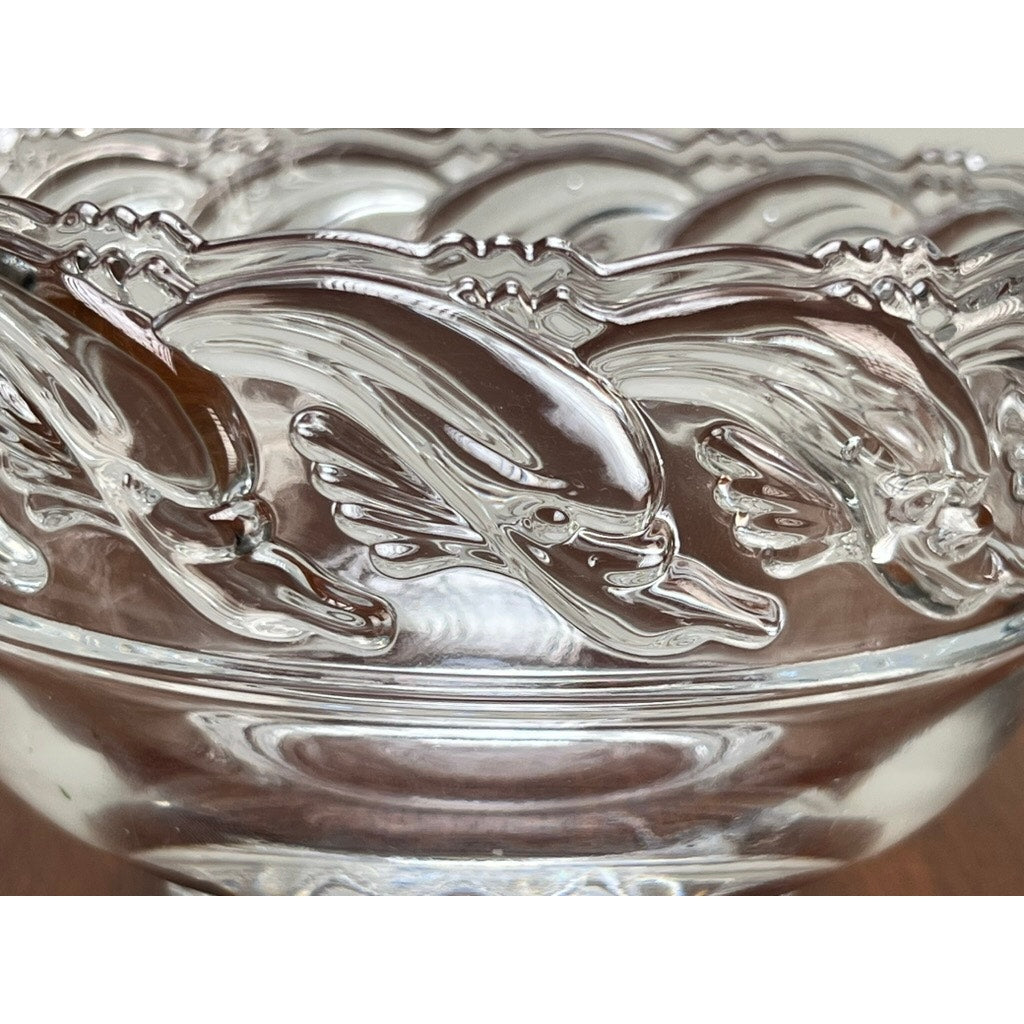 This Vintage Tiffany & Co. Mid-Century Modern Crystal Footed Bowl features a glossy finish and a decorative rim with an embossed repeating dolphin pattern, highlighting the brand's classic design.