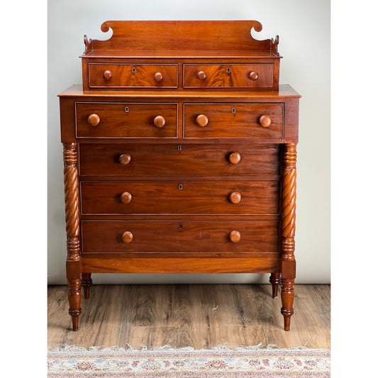 An Antique Federal Period Mahogany Sheraton Deck Top Chest of Drawers c. 1820 features five drawers, two small upper compartments, round knobs, turned legs, and a decorative top in early 19th-century American style on a wooden floor with part of a rug showing.