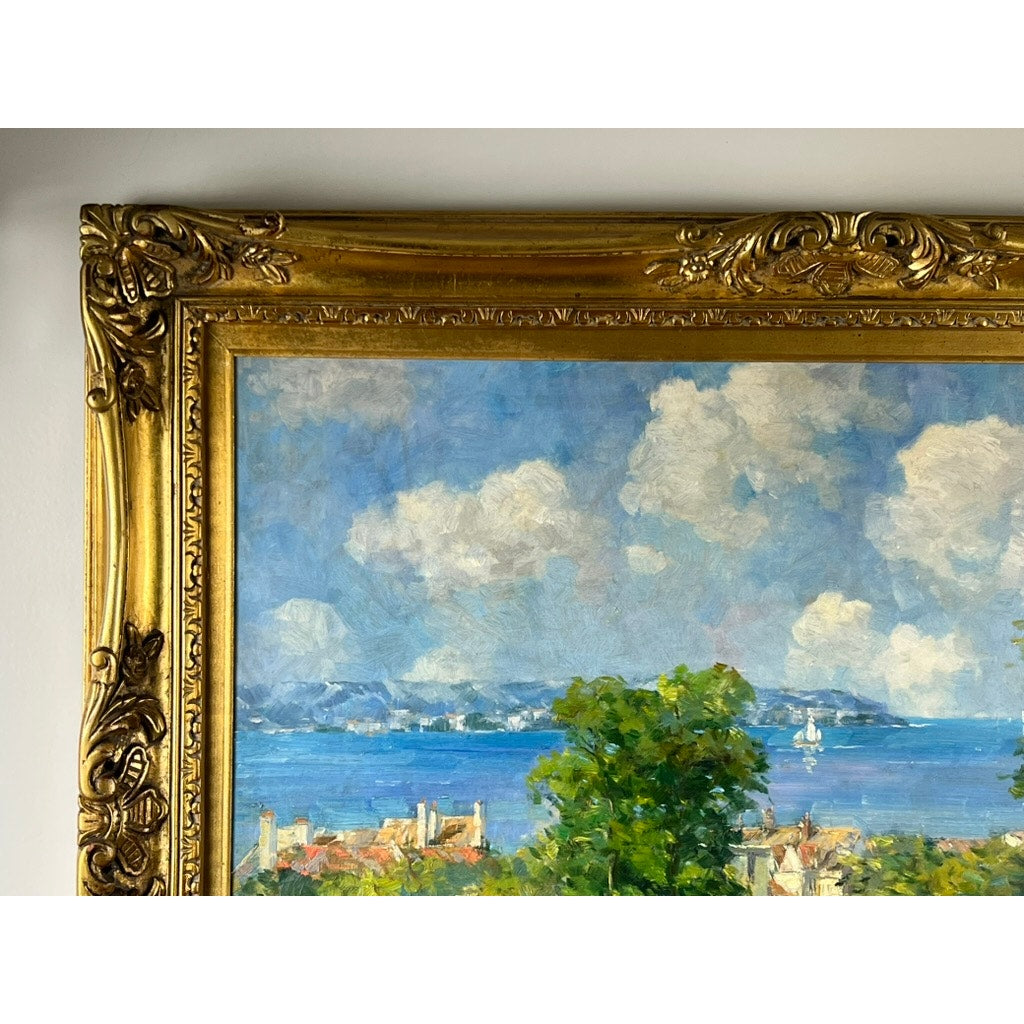Close-up of the top left corner of a gold ornate frame featuring a vintage oil on canvas impressionist painting of a summer coastal scene signed P. Maris, with blue sky, clouds, water, greenery, and rooftops. Brand unknown.