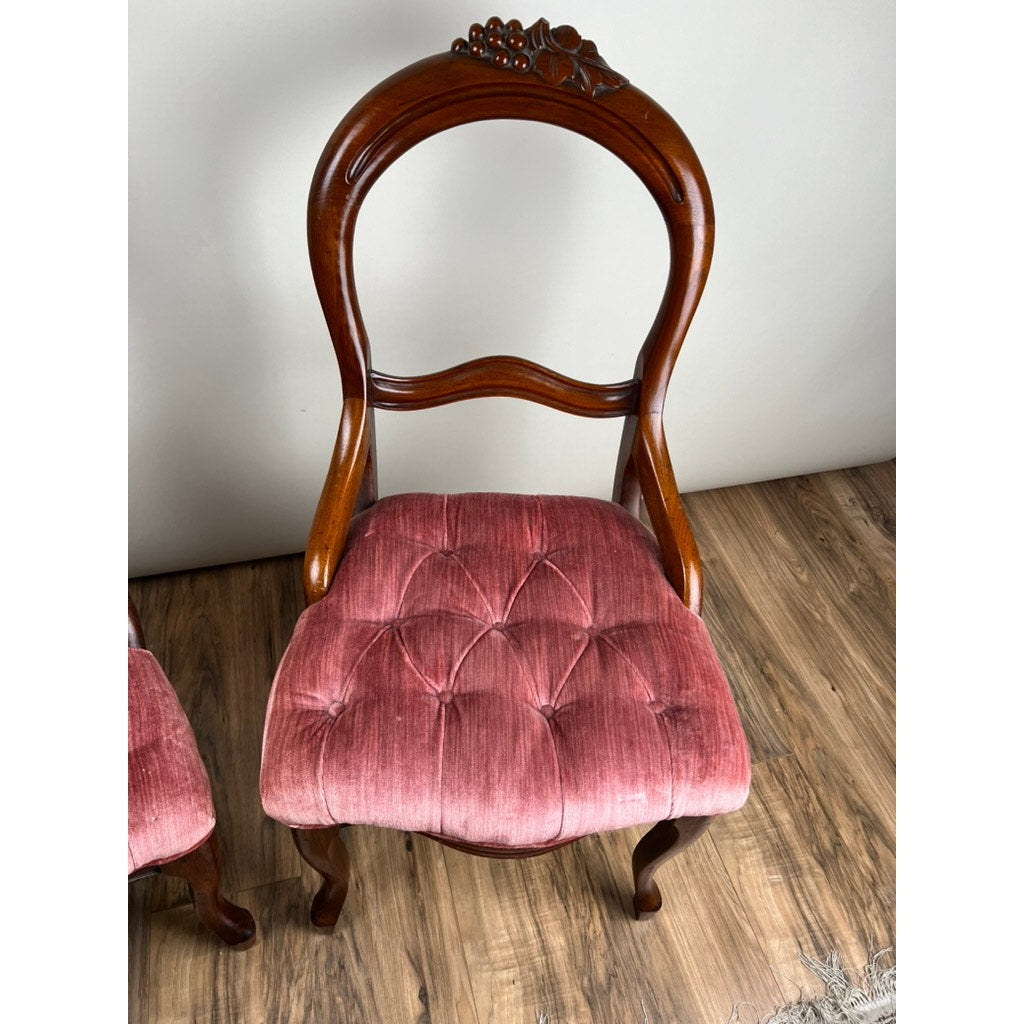 An Antique Pair of Victorian Walnut Balloon Back Tufted Side Chairs (c. Late 19th Century), with carved floral details and pink tufted velvet seats, sit on a wood floor against a light wall; brand: none/unknown.