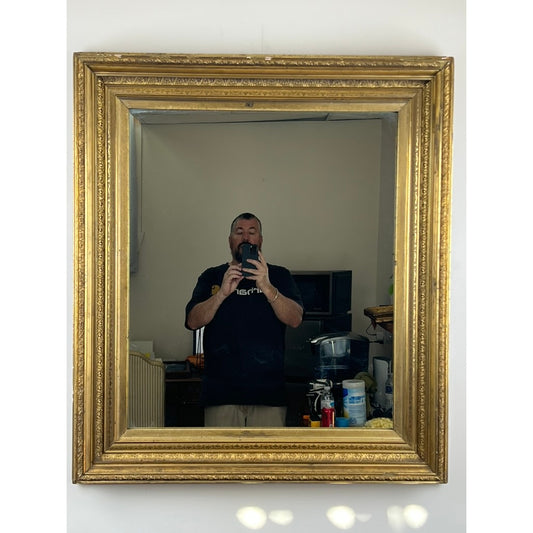 A person takes a selfie in the Fine Antique 19th Century Gilt Wood Mirror 39 x 34 by Pearl City Antiques, capturing their reflection and various background furnishings in its large, ornate frame.