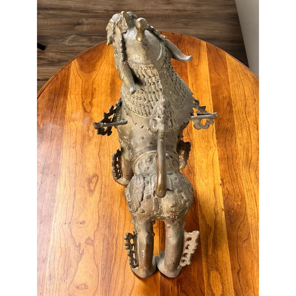 A Vintage 17” Cast Brass Pixiu Tibetan Lion c. 1960 sits on a polished wooden table. Photographed from above, the image highlights its ornate details and stylized form, evoking classic Asian and Tibetan Chinese decor. Brand: Unknown.