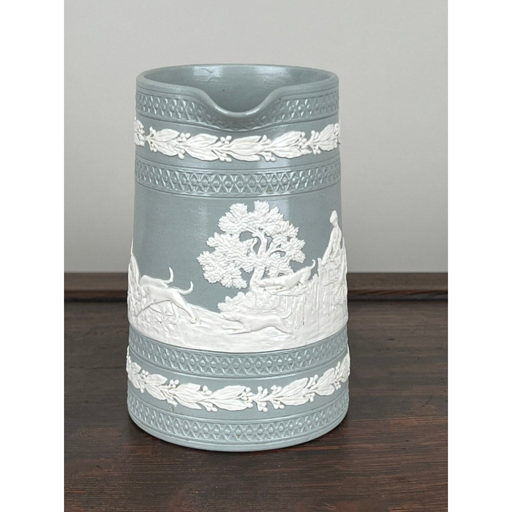 The Vintage Copeland Spode English Jasperware Fox Hunt Pitcher features blue-gray ceramic with raised white classical designs of figures, dogs, and trees, evoking a fox hunt scene. Displayed on a dark wooden surface. Brand: Copeland Spode.