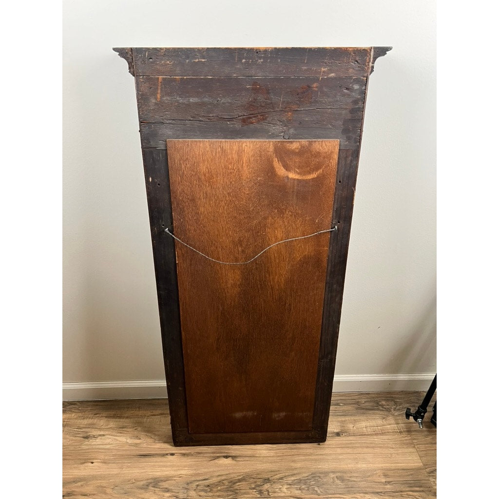 An Antique American Empire Mahogany Pier Mirror c. 1840 with a central dark wooden panel and hanging wire, stands upright on a wooden floor against a light-colored wall.