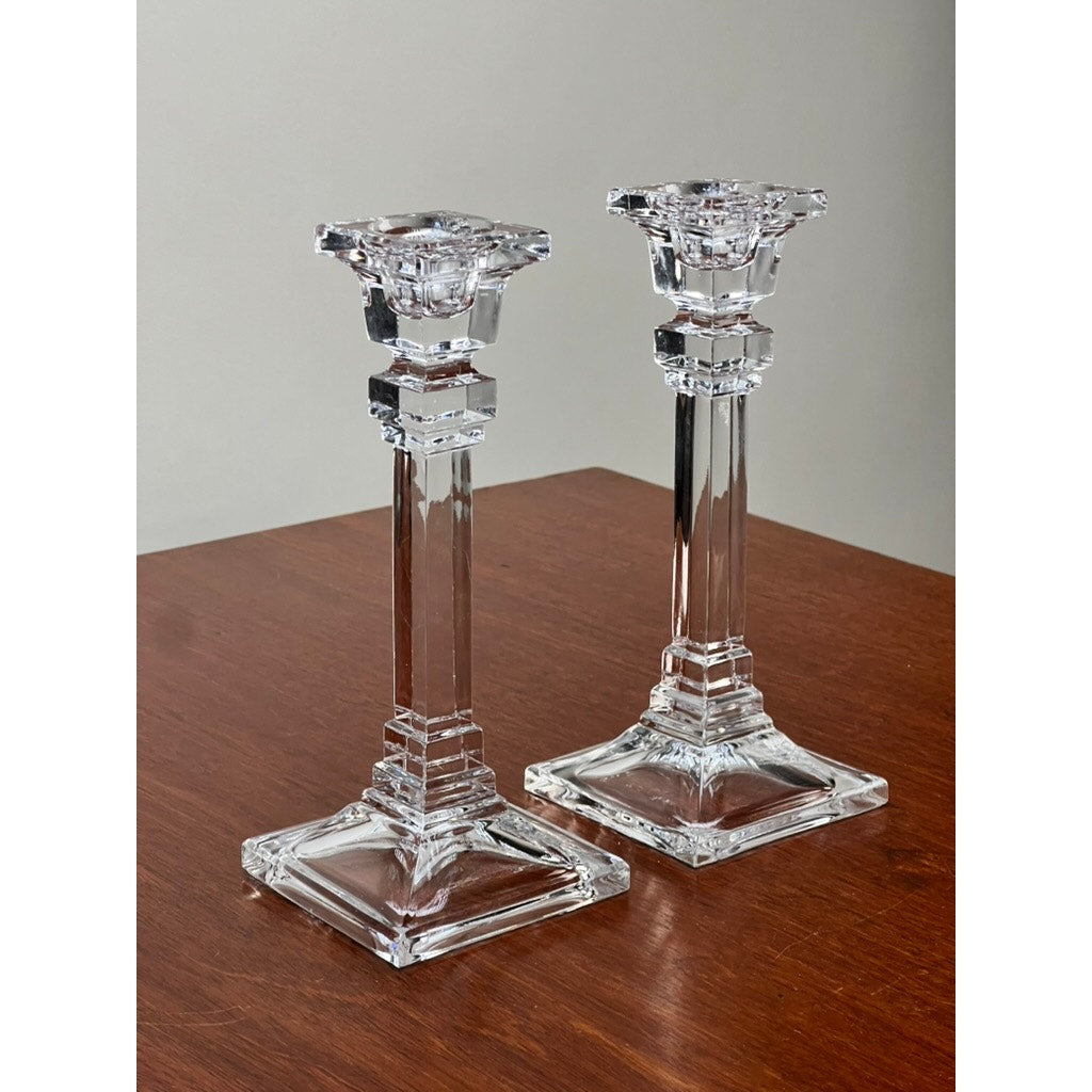 A Vintage Pair Tiffany & Co. Clear Crystal Candlesticks with geometric square bases and ornate tops are placed side by side on a polished wooden surface against a neutral background.