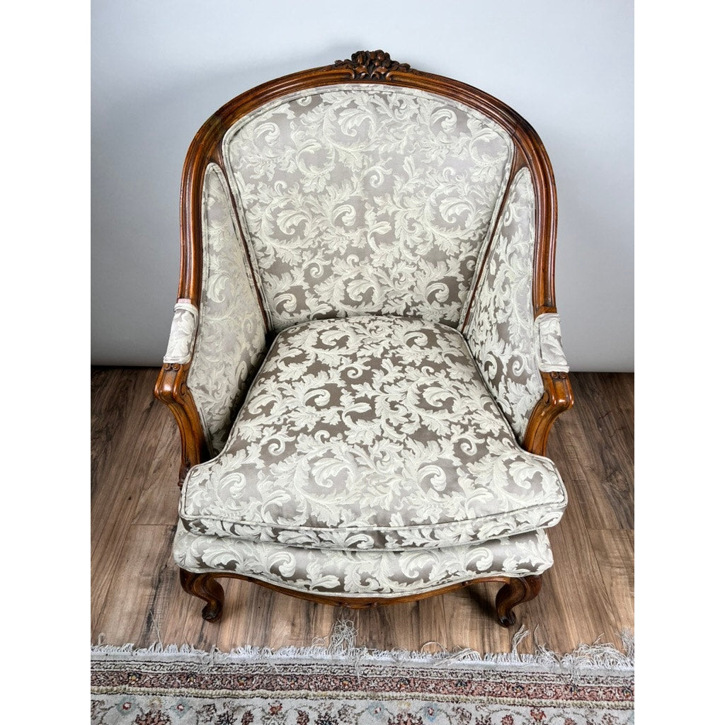 Antique French Louis XV Rococo style Bergère arm chair (mid-19th c.) with carved walnut frame and newer damask upholstery, set on a wooden floor beside a patterned rug. Brand: Unknown.