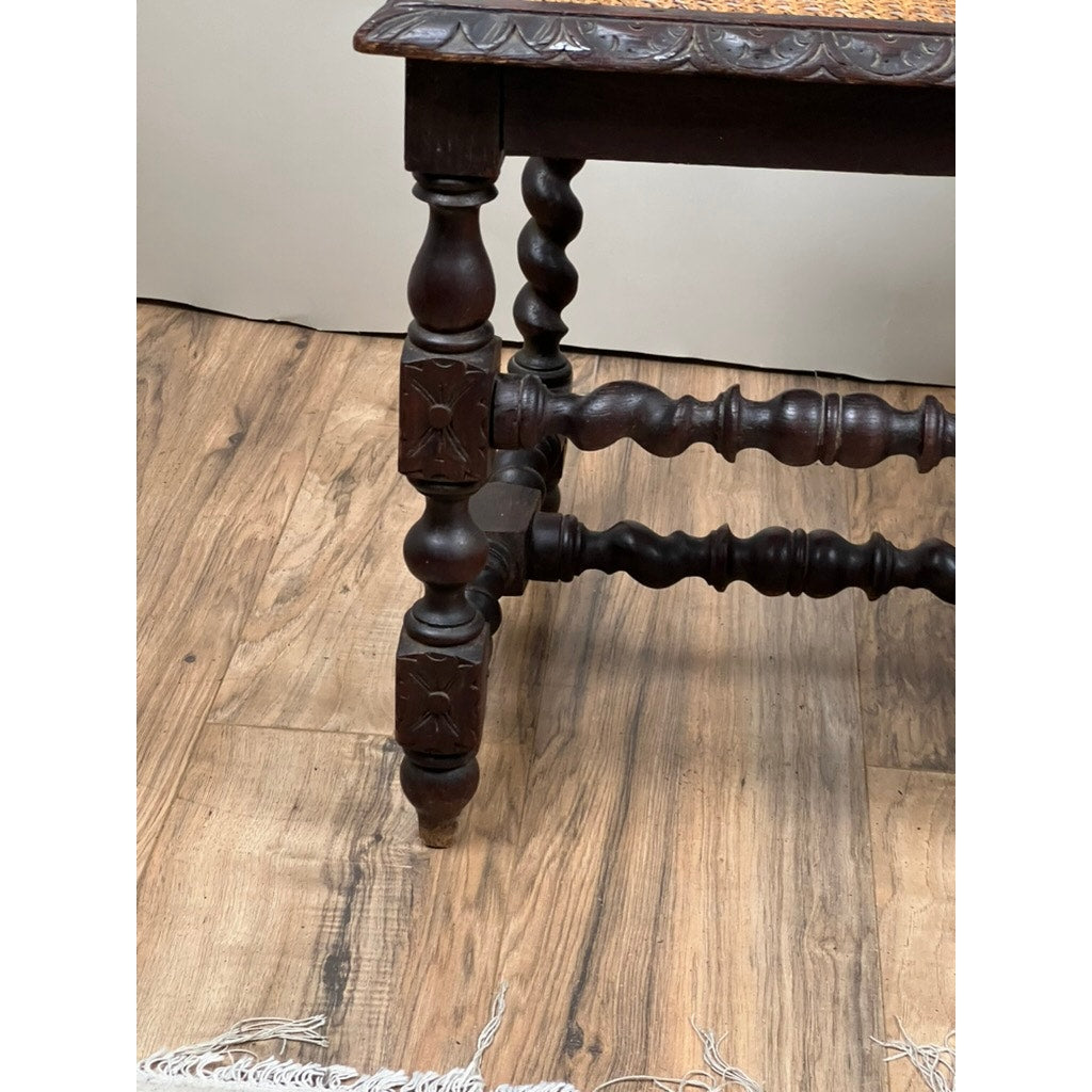 A close-up of an ornately carved, twisted leg from a Pair of Antique French Walnut Hunting Chairs (late 19th century) stands on a wood floor, with part of a white fringed rug visible in the corner. Brand: None/Unknown.