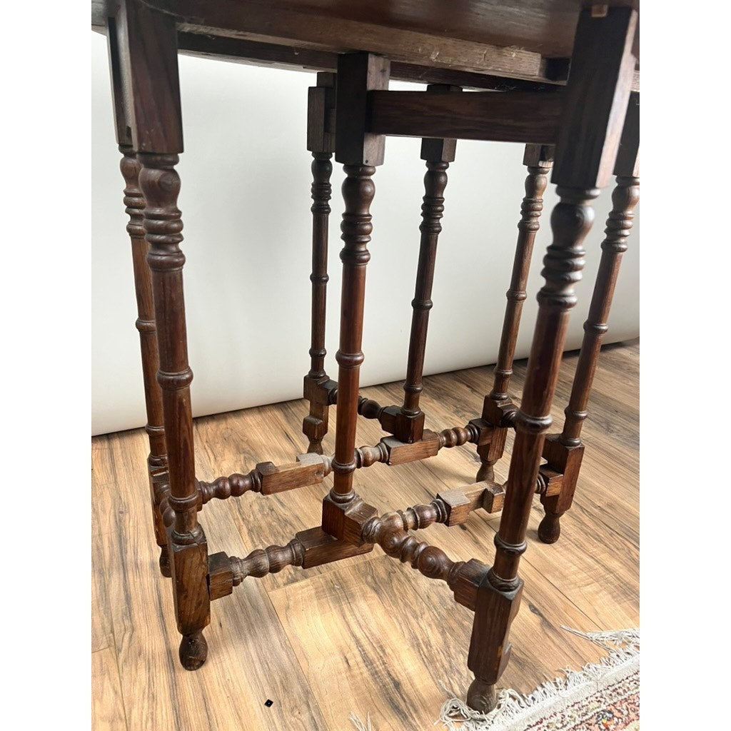 Close-up of the ornate, turned legs and crossbars on an Antique English Oak Carved Gateleg Occasional Table (late 19th c.), shown on a wood floor with a patterned rug partly visible at the bottom right.