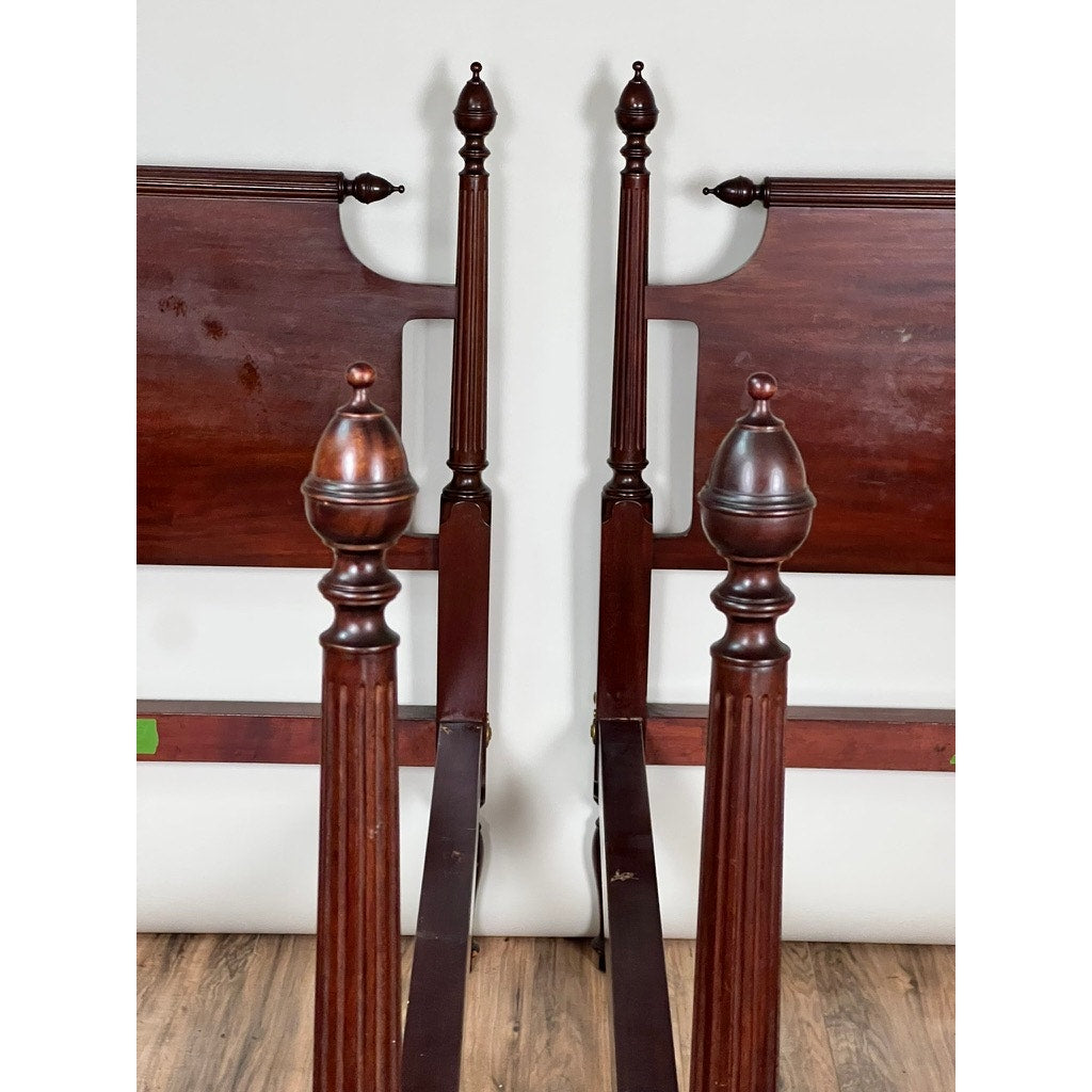 A vintage pair of Centennial solid mahogany twin four poster beds (c. 1940), featuring tall turned posts and decorative finials, sit side by side on a wood floor against a plain white wall, evoking classic Federal Sheraton style.