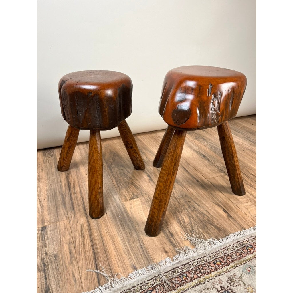 A pair of vintage live edge Wabi Sabi cherry stools, signed by Neil Panyik, with rounded seats and splayed legs, rest on a wooden floor beside a patterned rug, showcasing natural artistry and unique craftsmanship.