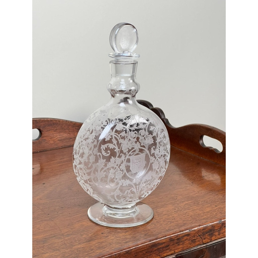 A Vintage Baccarat "Michelangelo" Crystal Decanter for Martell Cognac, c. 1930, with an etched floral design and round stopper, displayed on a polished wooden surface against a plain light background.