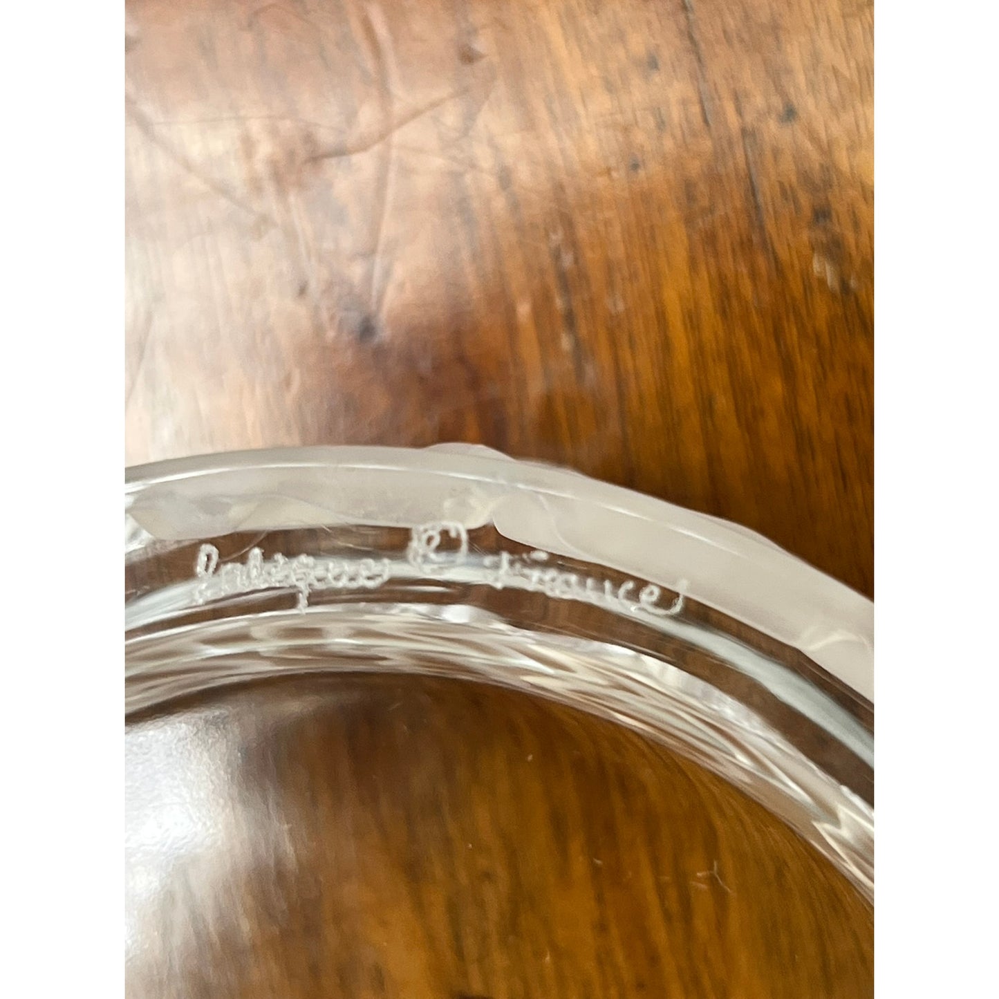 A close-up of the rim of a Vintage Lalique Crystal Enfants Box by Lalique, with "Lalique France" engraved and set on a wooden surface—an exquisite example of French art glass.