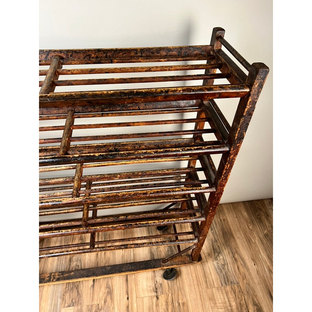 An Antique Oak Shoe Factory Rolling Rack on original industrial casters (late 19th century) stands on a wooden floor by a plain light wall, featuring multiple open shelves with horizontal and vertical bars and a worn, rustic finish.