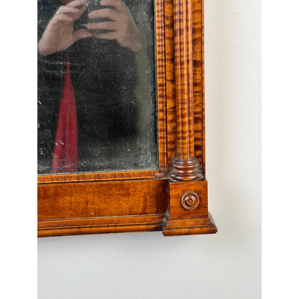 A close-up of a Fine Antique Federal Period Tiger Maple Two Panel Mirror c. 1820 shows part of a person’s reflection, including their hand holding a phone and a red scarf, in the ornate frame; brand unknown.