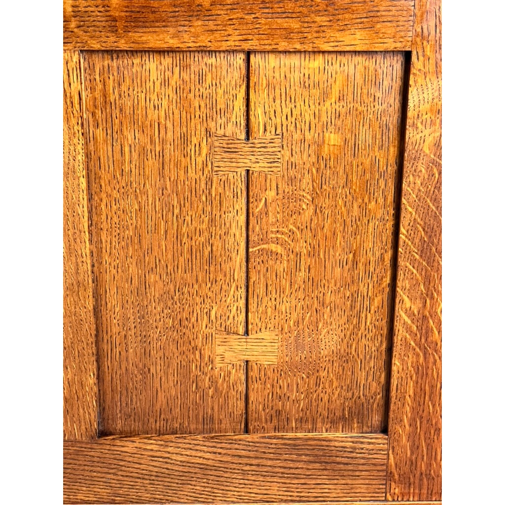 A close-up of the Stickley Vintage Harvey Ellis Millennium Edition Oak Blanket Chest shows its central bowtie inlay, highlighting rich wood grain and craftsmanship with a warm golden-brown finish, echoing classic Arts & Crafts style.