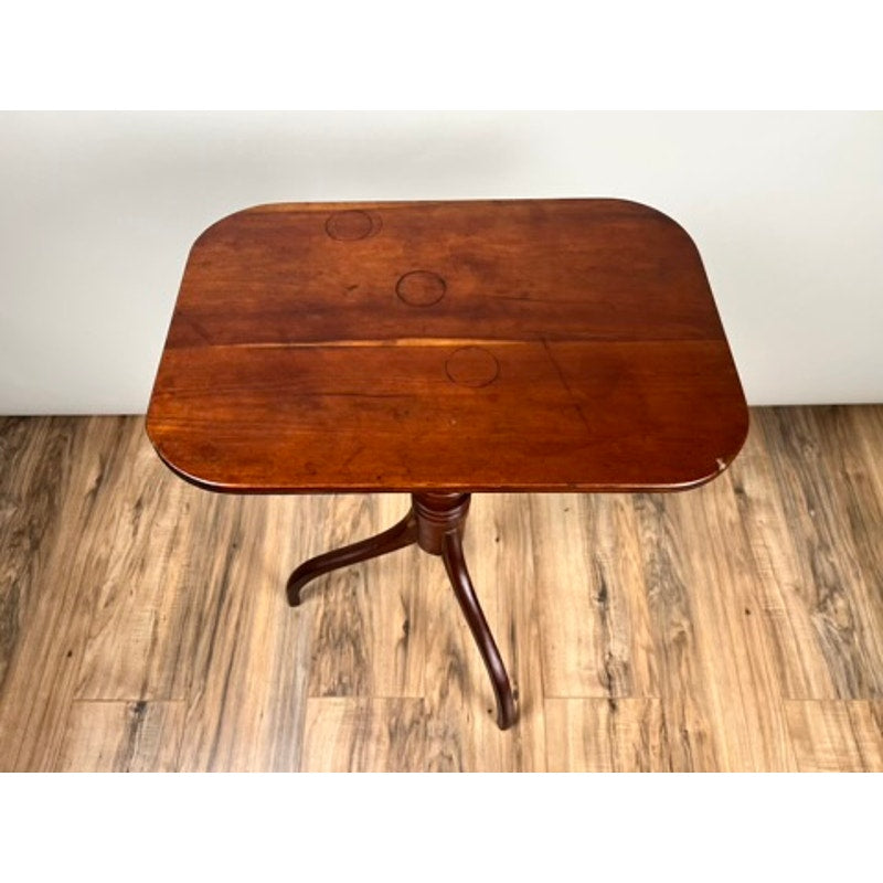 An Antique Federal Period Cherry Hepplewhite Candle Stand (mid-19th century) with a rectangular top, rounded edges, and signs of wear stands on three curved legs against a plain wall on a wooden floor. Brand: None/Unknown.