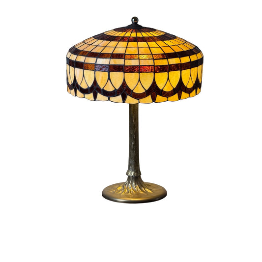 A Vintage Tiffany Revival Leaded Stained Glass Table Lamp with a cast brass tree-form base, featuring a shade in yellow, orange, and red patterns, photographed on a white background.