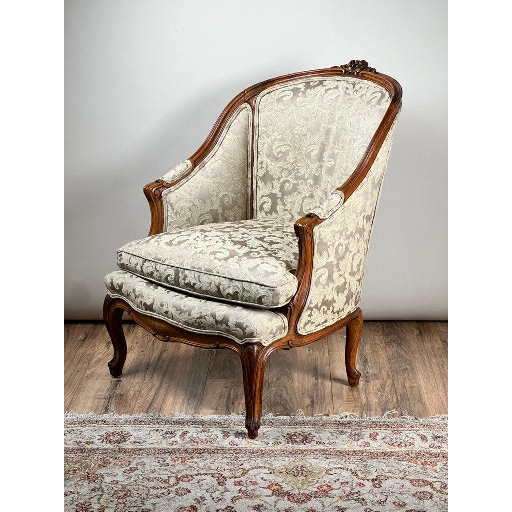 An Antique French Louis XV Rococo Style Bergère Arm Chair with newer damask upholstery (mid 19th century) sits on a wooden floor next to a decorative, patterned rug. Brand: None/Unknown.
