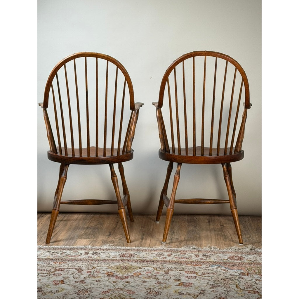 A pair of signed L.E. Partridge Connecticut bench-made continuous-arm Windsor chairs from the 1960s are arranged side by side on a patterned rug against a plain, light-colored wall, evoking the timeless elegance of early American furniture.