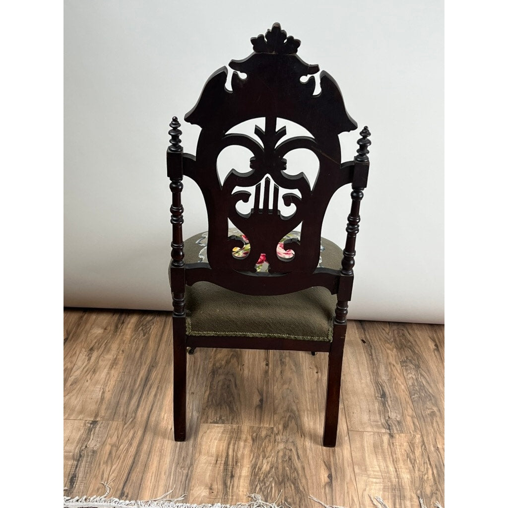 An Antique Victorian Rococo Revival carved walnut slipper chair with a floral needlepoint seat (late 19th century) stands on a wooden floor against a plain light background. Brand: None/Unknown.
