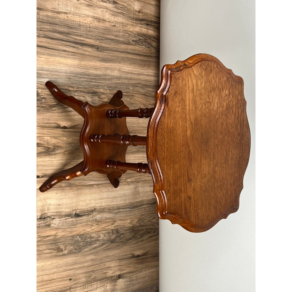 An Antique Victorian Walnut Turtle Top Candle Stand from the late 19th century, featuring a small round top and three ornate legs, sits on a wood-patterned floor beside a light-colored wall.