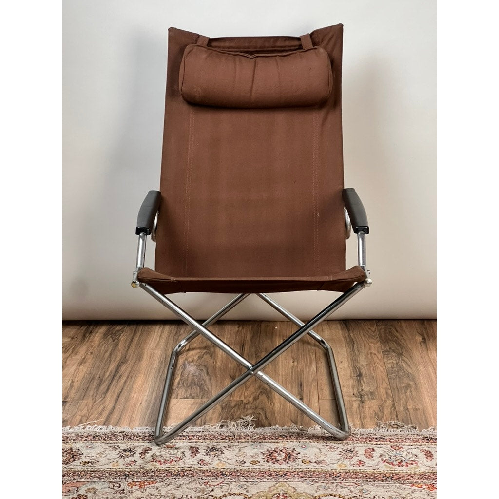 The Vintage Uchida Z Chair Japanese Modern Chrome Sling Lounge Chair with Headrest by Uchida is a brown fabric lounge chair featuring black armrests and a cantilevered chrome frame, inspired by Japanese modern design. It is shown placed on a wooden floor, with part of a patterned rug visible at the bottom.