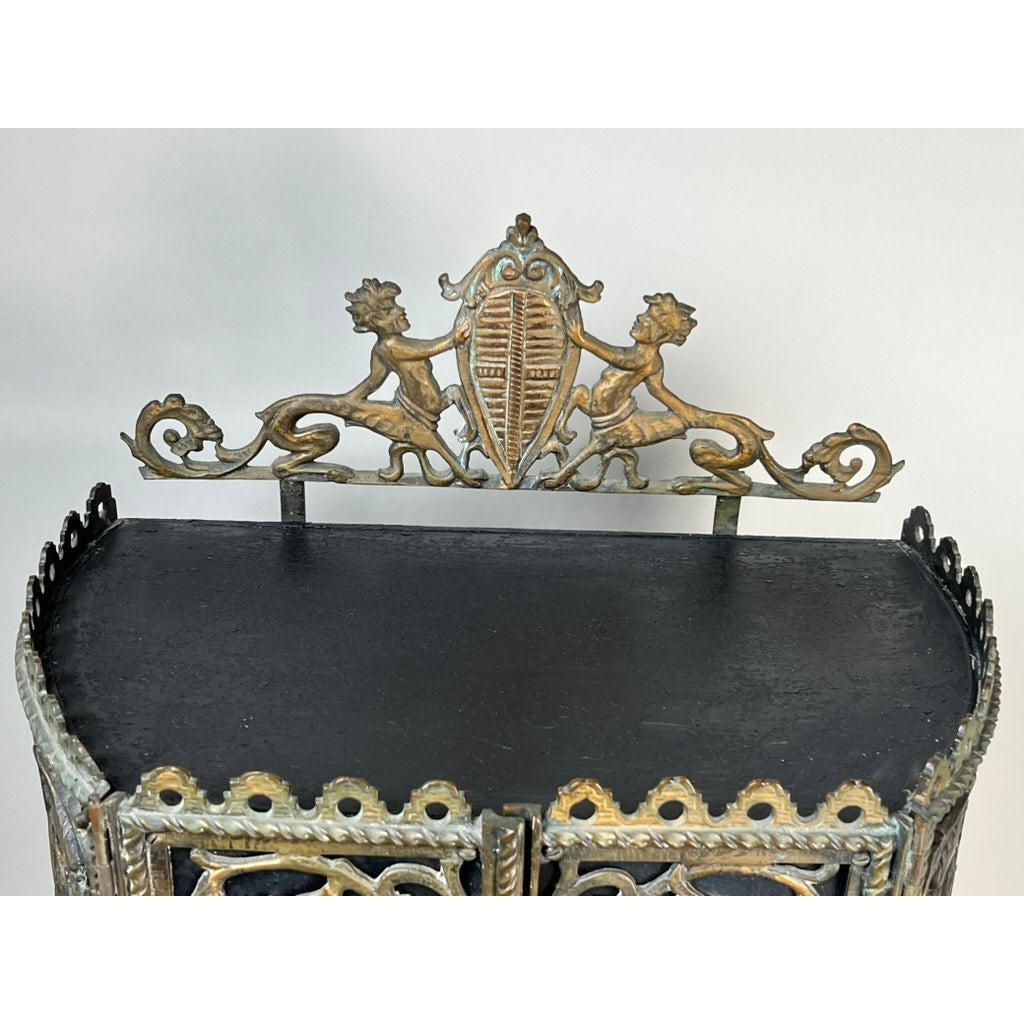 Antique Gothic Revival cast iron and brass phone stand, attributed to Oscar Bach or Bertram Segar c. 1920 Greenwich Village, features a decorative crest with two cherubs, ornate scrollwork, and a black lower surface. Brand unknown.