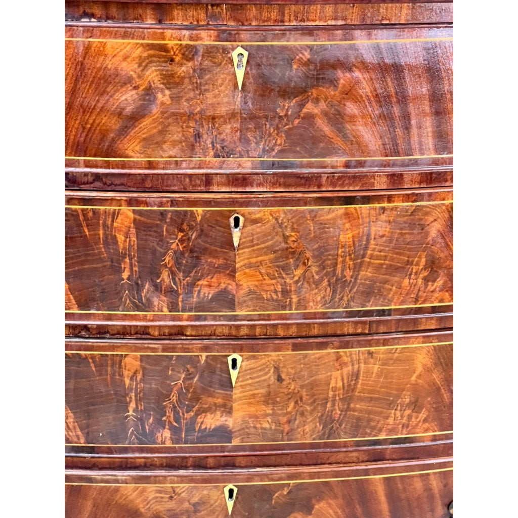 Close-up of four curved drawers from an Antique Sheraton Mahogany Bowfront Chest (early 19th century), featuring decorative grain patterns, brass keyhole escutcheons, thin inlaid borders, and a glossy mahogany finish. Brand: Unknown.