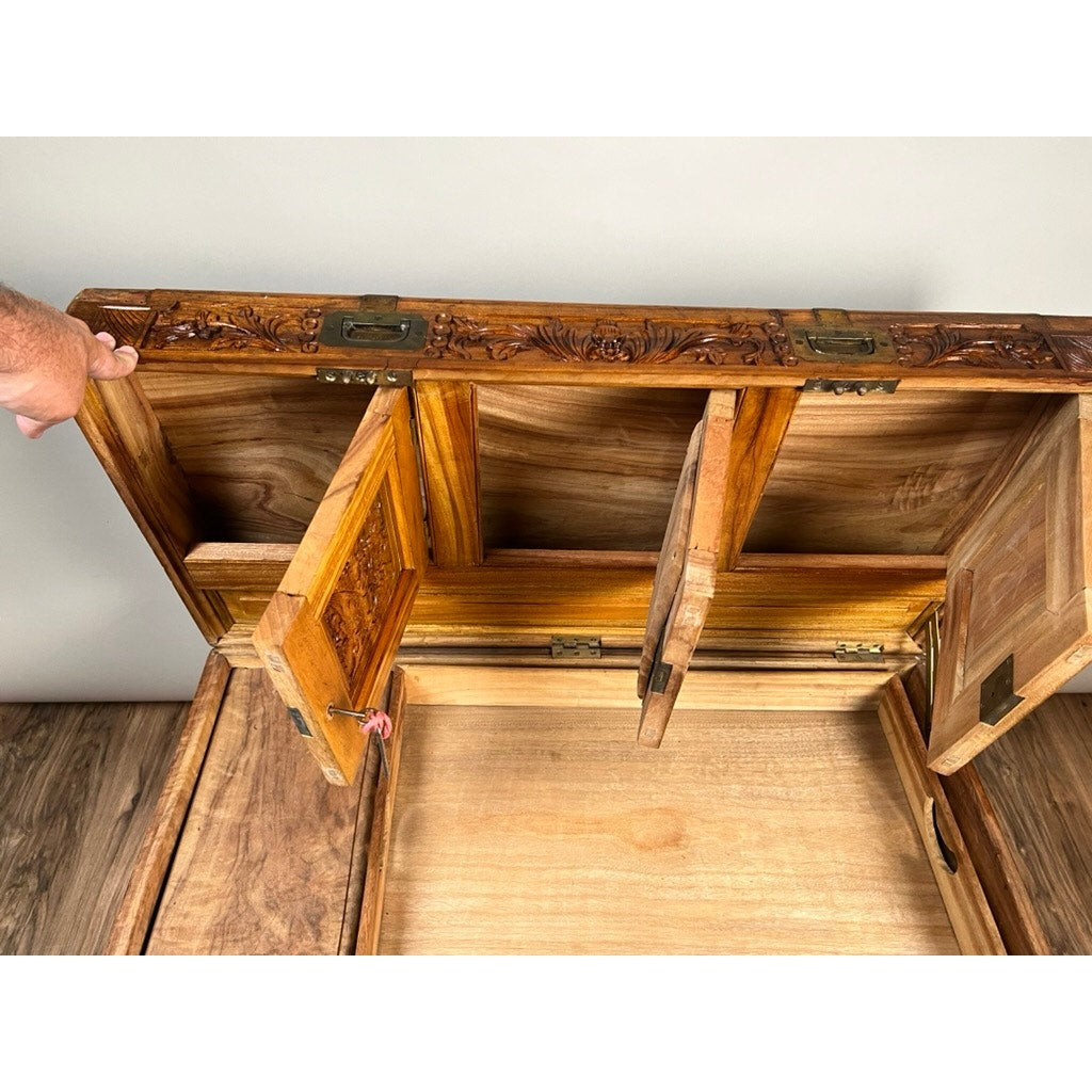 A hand opens the intricately carved lid of the Chinese Export Carved Camphor Wood Dowry Chest, revealing three smaller hinged compartments inside. Both the interior and exterior display a natural wood finish.