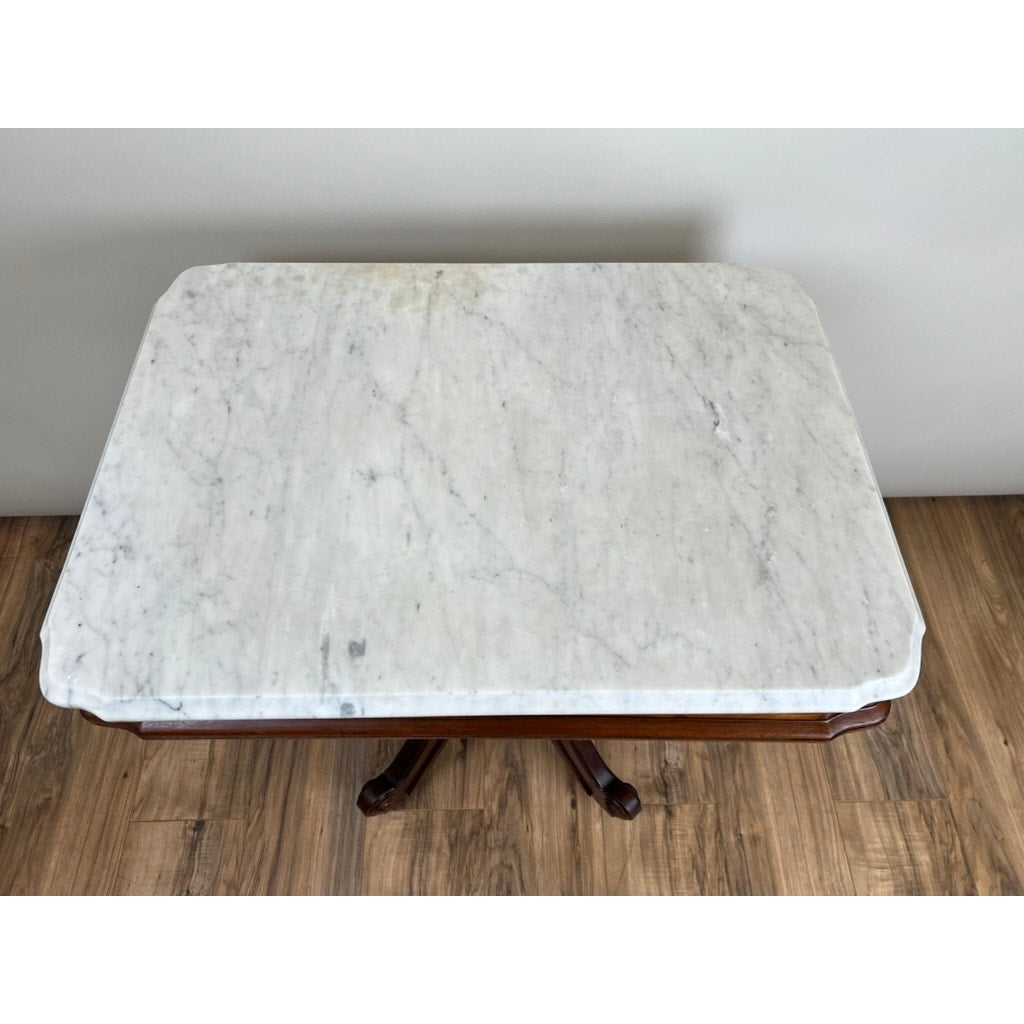 An Antique Eastlake Victorian Walnut Marble Top Stand, late 19th century, features a white marble surface with gray veining and a dark walnut pedestal base, shown on a wood floor against a light-colored wall.