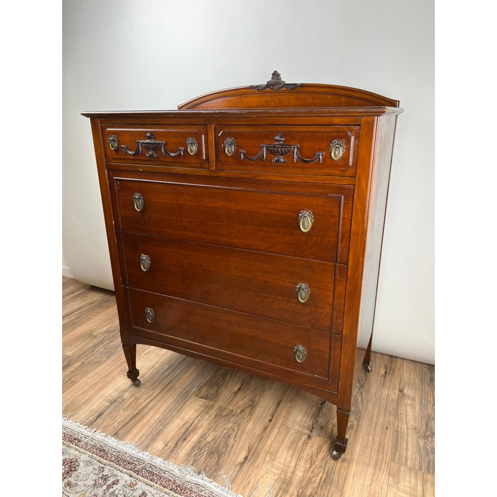 Antique Depression Era Mahogany Two Over Three Chest of Drawers c. 1930s with five drawers, decorative carvings, ornate brass handles, and four legs with small wheels; displayed on a wood floor against a light-colored wall. Brand: Unknown.