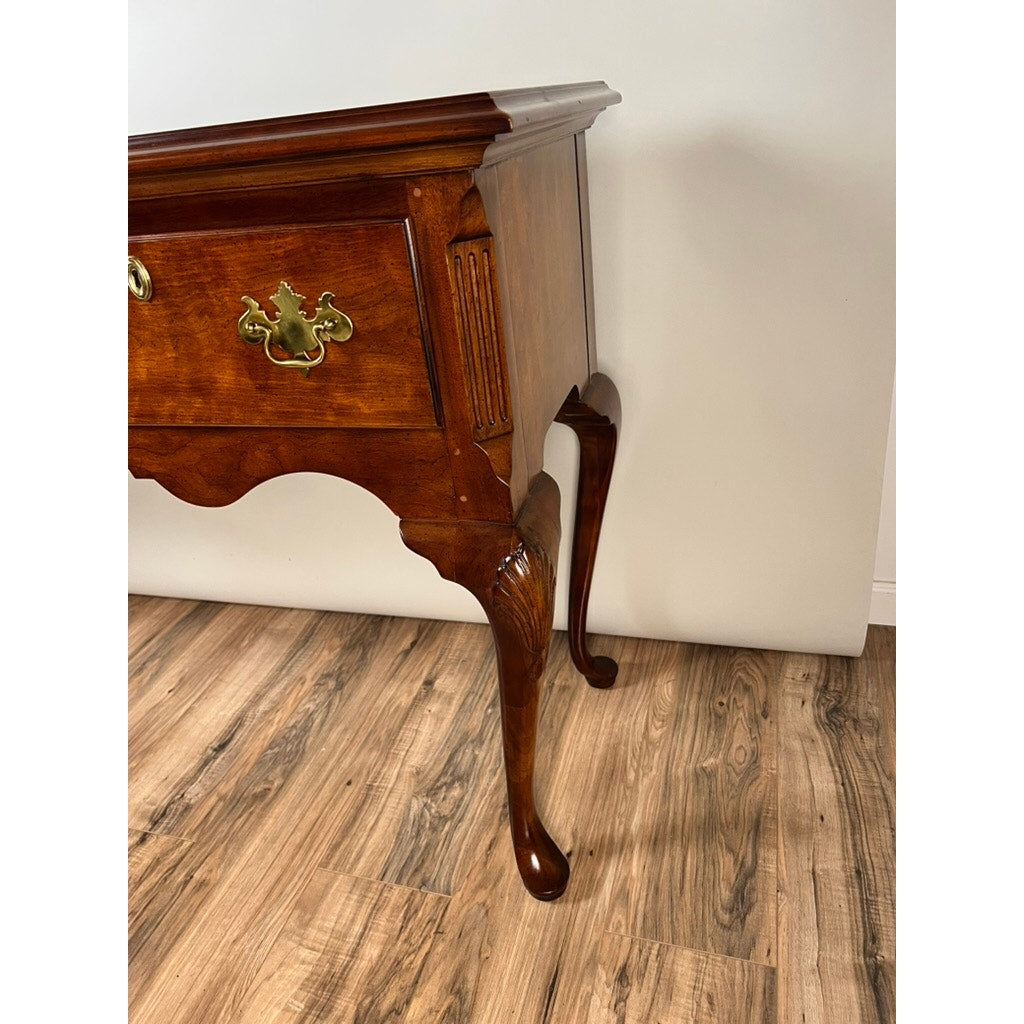 A close-up of the Vintage Solid Cherry Queen Anne Style Sideboard by Henredon, featuring ornate brass hardware and carved legs, stands on a wood-patterned floor against a white wall.