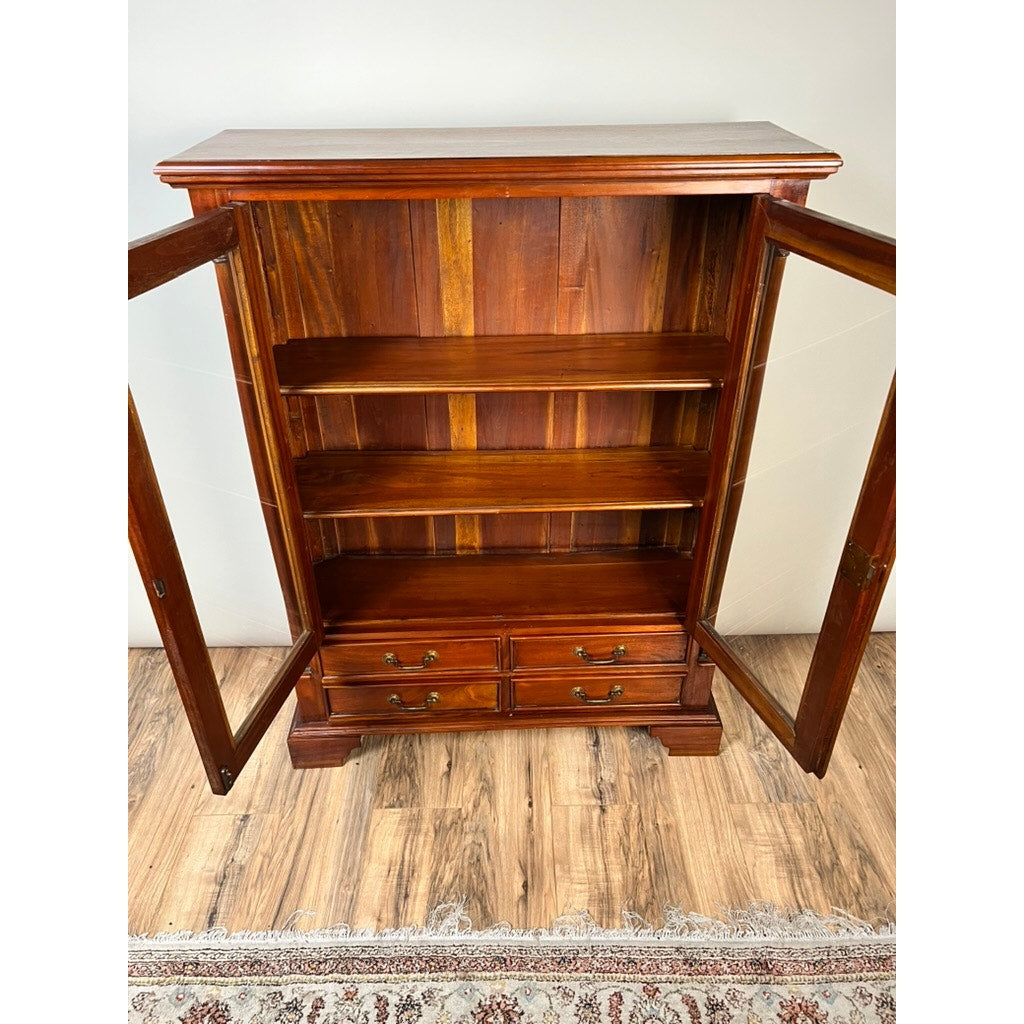 The Vintage Victorian Style Glass Door Mahogany Bookcase features two spacious shelves and four drawers behind its elegant doors, standing on a wooden floor next to a patterned rug.