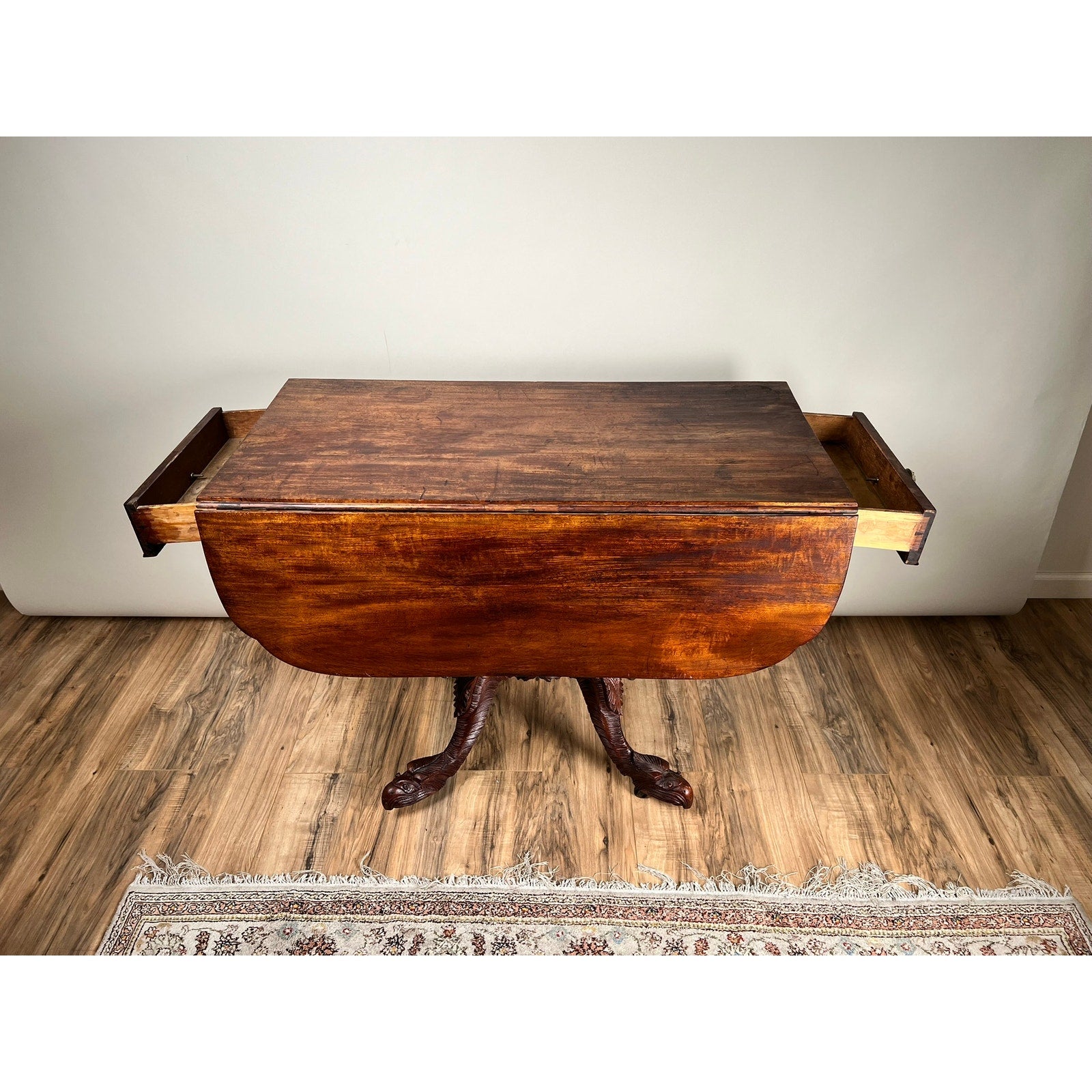 Antique American Empire Drop Leaf Table with Great Eagle Carved Feet c. 1840, featuring drop leaves and two drawers, displayed on a wooden floor near a patterned rug. Brand: Unknown.