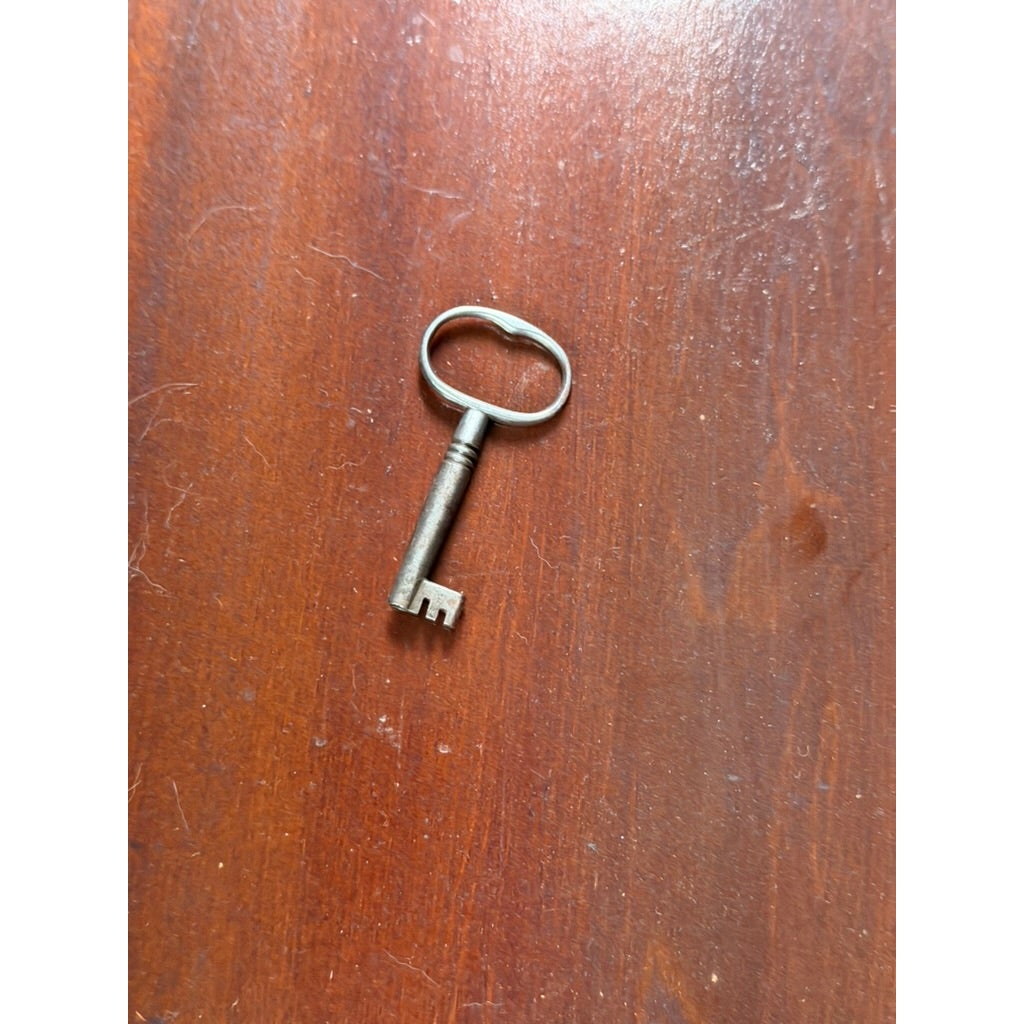 A vintage metal key with an oval bow resting on the mahogany surface of a New York Classical Revival Carved Mahogany Double-Pedestal Library Table, labeled Ernest F. Hagen, circa 1890–1925.